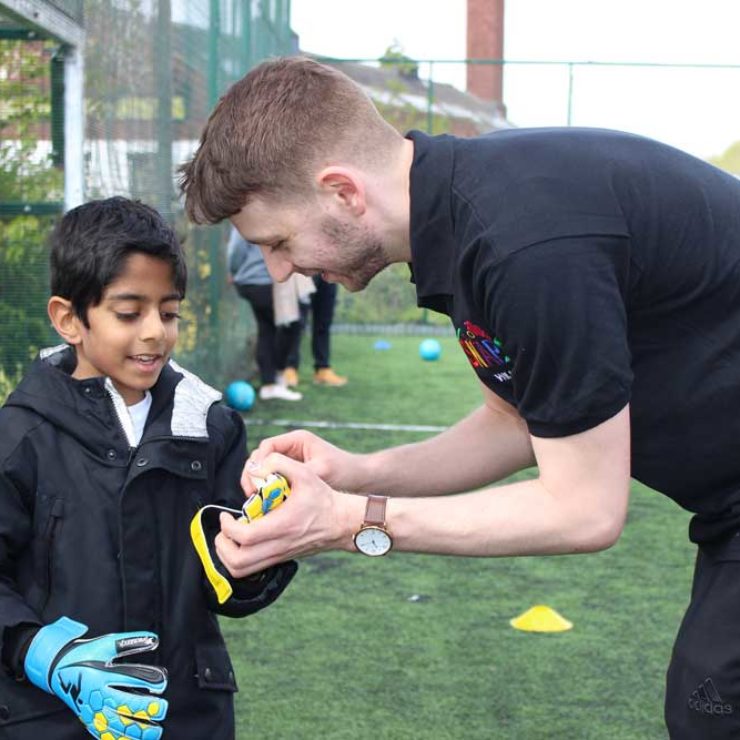 Young boy being helped by an instructor to put his goalie gloves on