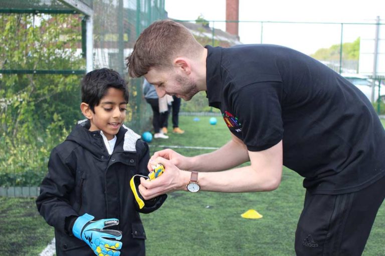 Young boy being helped by an instructor to put his goalie gloves on