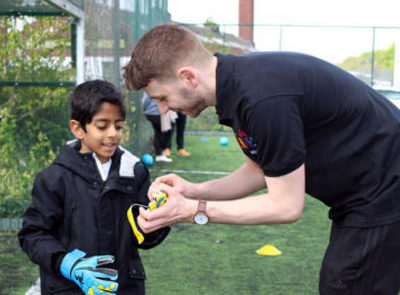 Football instructor helping a young boy with his gloves