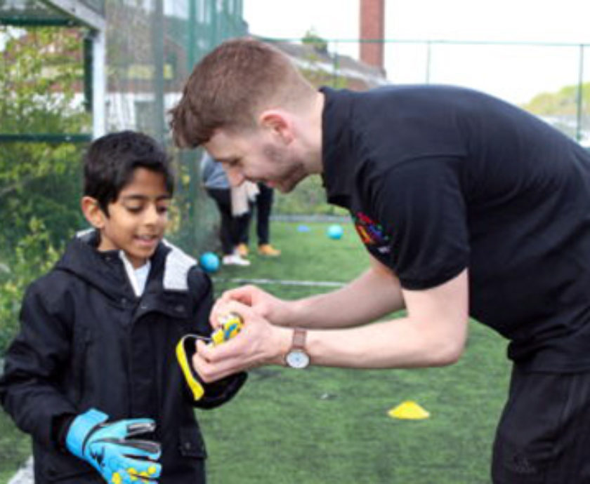Football instructor helping a young boy with his gloves