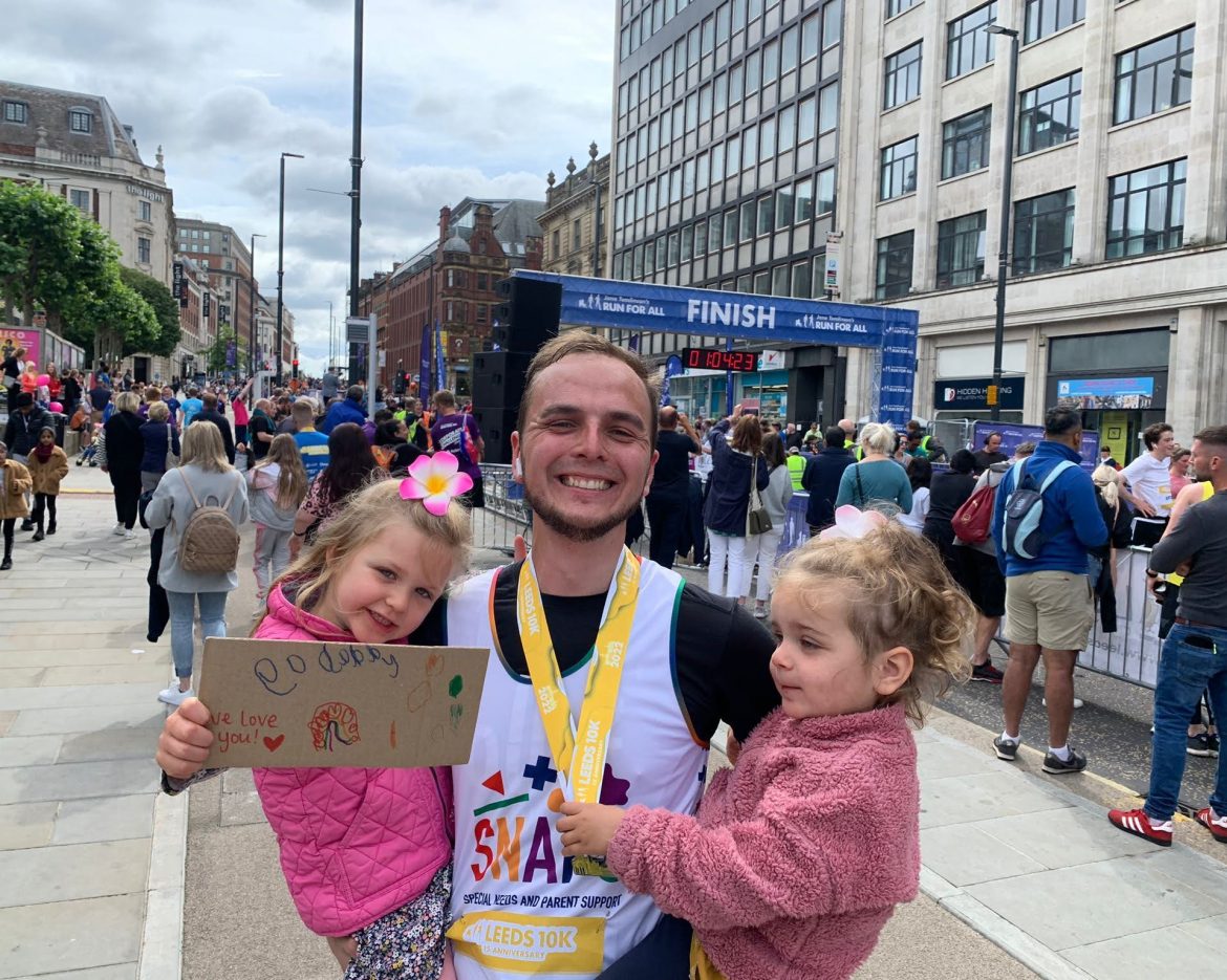 A father in a SNAPS t-shirt celebrating with his two daughters after running the 10k