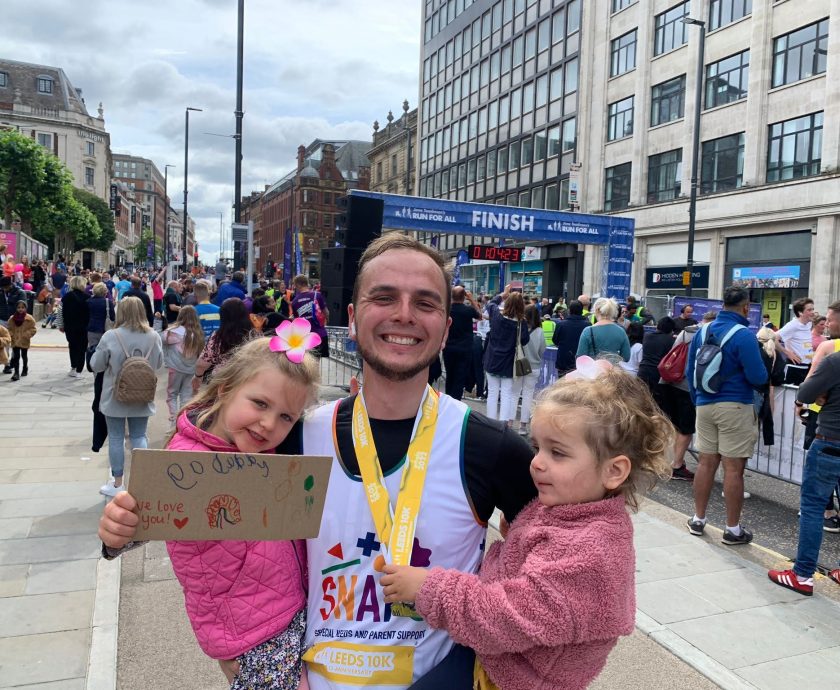 A father in a SNAPS t-shirt celebrating with his two daughters after running the 10k
